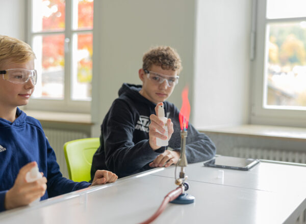 Zwei Mittelstufenschüler mit Schutzbrille führen einen Versuch mit dem Flammenbild des Bunsenbrenners durch.
